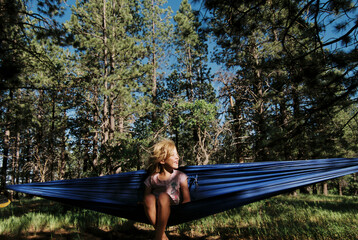 Cheerful girl resting in hammock against trees at forest