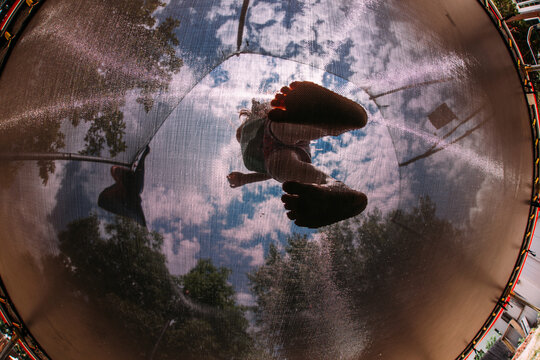 Directly below shot of girl standing in trampoline against cloudy sky at playground