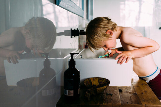 Side view of shirtless boy spitting while brushing teeth