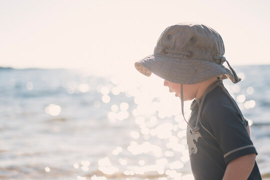 Side view of boy wearing hat while standing at beach against sea during sunny day