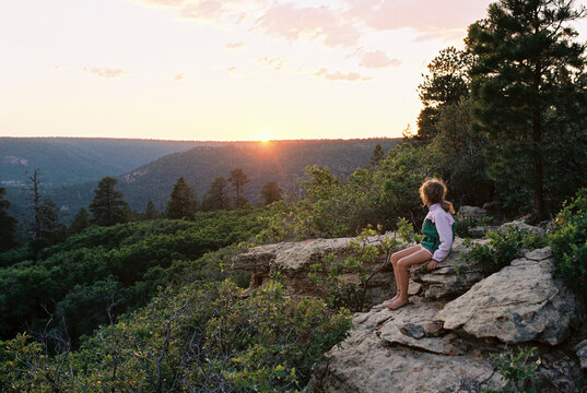 Girl looking at view while sitting on rocks during sunset