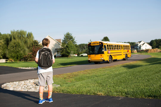 Rear view of boy with backpack waiting for school bus against clear sky at lawn