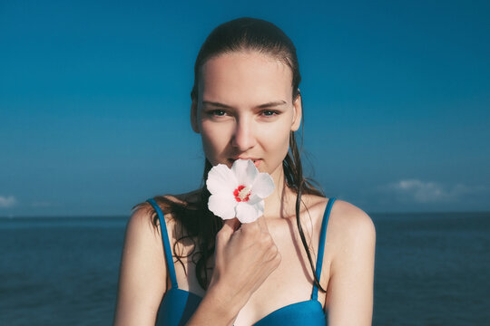 Portrait of woman holding hibiscus against sea and sky