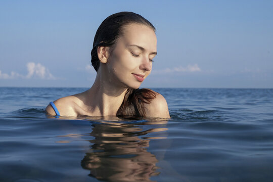 Happy woman with eyes closed swimming in sea against sky