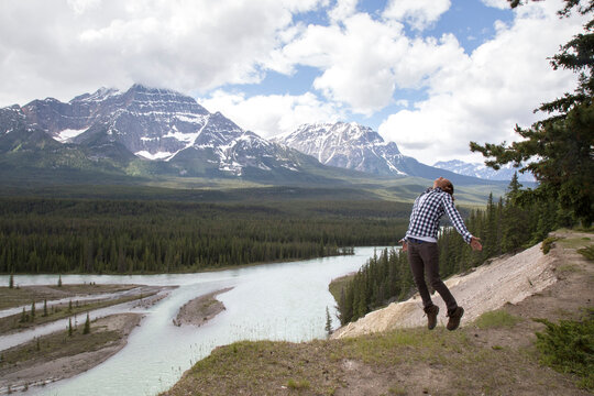 Excited hiker jumping against mountains and cloudy sky