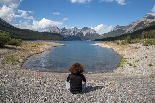 High angle view of hiker meditating while sitting at lakeshore against mountains and cloudy sky