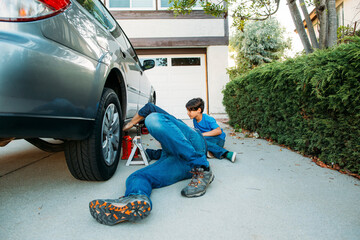 Father teaching son to repair car while lying down at driveway