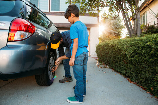 Son looking at father tightening tire with spanner at driveway