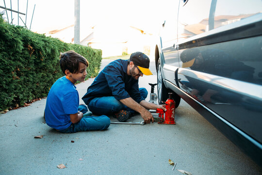 Father teaching son to use car jack while sitting at driveway