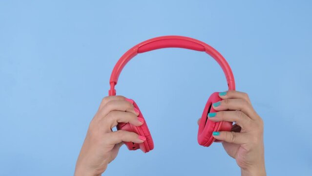 Female hands holding headphones on pastel blue background in studio. Body language concept. With place for text or image, promotional content.