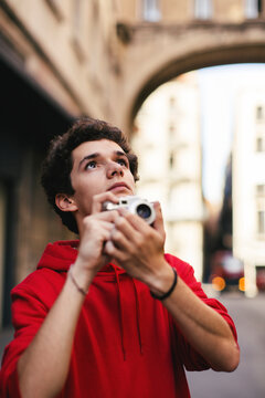 Teenage boy looking up while holding camera in city