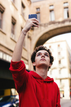 Low angle view of teenage boy photographing with smart phone while standing in city