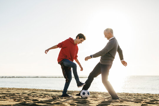 Full length of father and son playing soccer at beach against clear sky