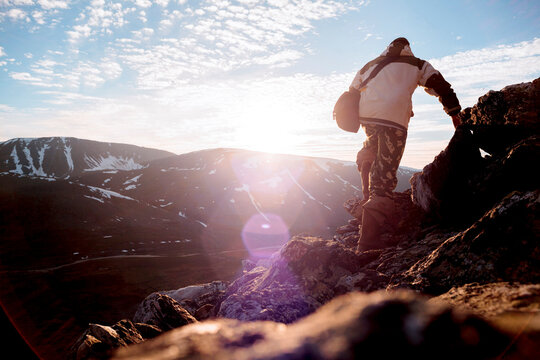 Rear view of hiker standing on cliff against sky during sunny day
