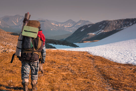 Rear view of hiker with backpack walking on field against snowcapped mountains