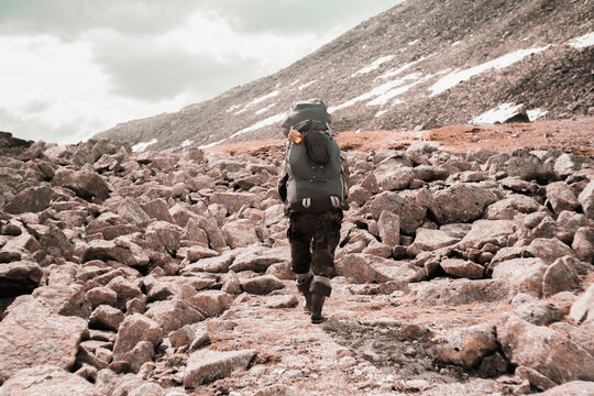 Rear view of hiker with backpack walking on rocks during winter
