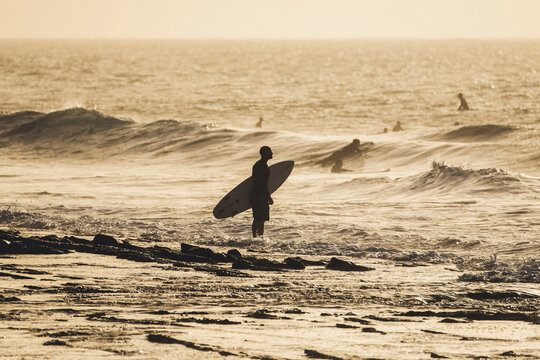 Silhouette man with surfboard standing in sea against sky during sunset