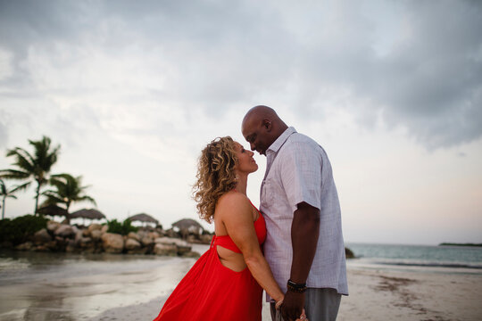 Couple standing face to face at beach against cloudy sky