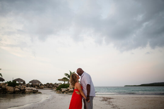 Side view of couple standing face to face at beach against cloudy sky