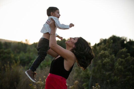 Side view of playful mother lifting son on field
