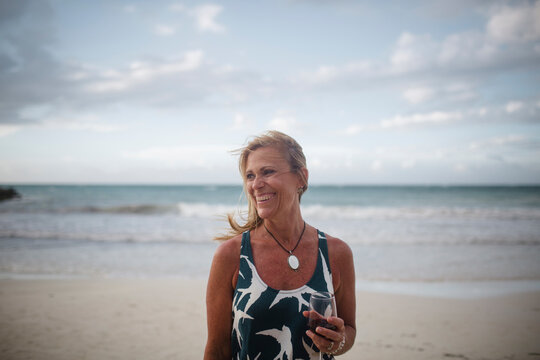 Cheerful woman holding wineglass while standing at beach