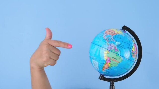 Female hands holding the globe and pointing on pastel blue background in studio. Body language concept. With place for text or image, promotional content.