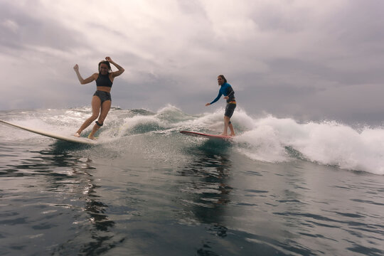 Friends surfing on sea against cloudy sky