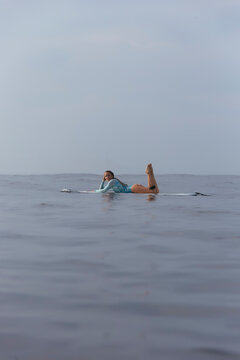 Side view of carefree woman lying on surfboard in sea against sky