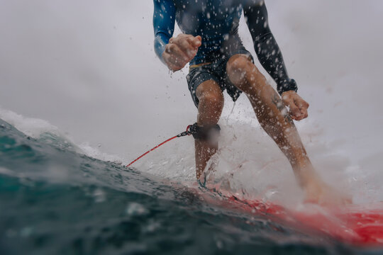Low section of man surfing on sea against cloudy sky
