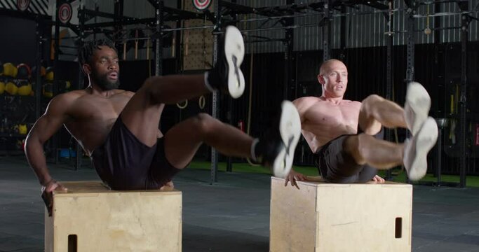 Slow motion. two muscular multiethnic shirtless fit Men doing Part of His Cross Fitness Training Plan Intense Workout, smiling athletes sit on box, do bicycle exercises, raising, lifting legs