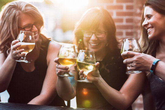 Cheerful female friends toasting beer while sitting at sidewalk cafe during sunny day