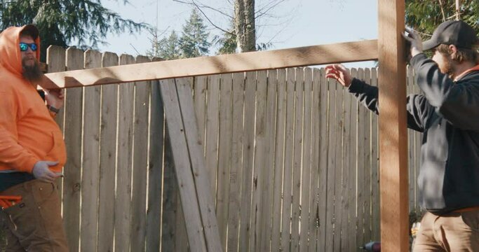 Two male construction workers discuss where to place 2x4 crossbeam on new cedar outdoor fence