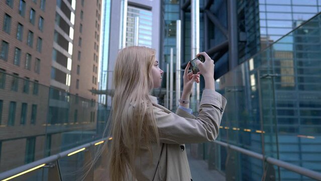 stylish blond girl using smartphone in the city, taking pictures. Girl using phone photography in downtown skyscraper street in Tokyo