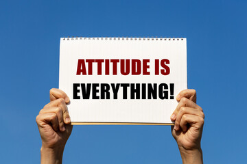 Attitude is everything text on notebook paper held by 2 hands with isolated blue sky background. This message can be used as business concept about attitude.
