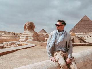 Stylish man against the background of the Giza pyramids complex. Clear, sunny day, blue sky. Vacation and travel concept