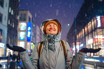 Obraz premium snowfall woman in a blue jacket and yellow hat christmas outside, city portrait in snowfall, young model posing in Dusseldorf city, fabulous advent evening