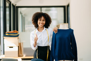 Calm curly brunette dark skinned woman on desk in office of fashion designer and holds tablet and smartphone...