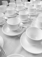 Many rows of white ceramic coffee or tea cups. Lines of coffee cups in front of conference room. White ceramic cups and saucers laid out on a buffet table at a catered event for serving a hot beverage
