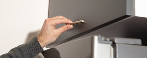 Male hand opening kitchen cupboard door.