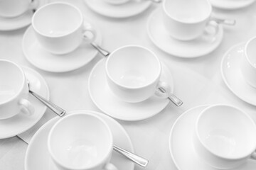 Many rows of white ceramic coffee or tea cups. Lines of coffee cups in front of conference room. White ceramic cups and saucers laid out on a buffet table at a catered event for serving a hot beverage