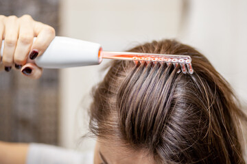 Woman uses darsonval for massage head's skin. Receiving electric darsonval facial massage...