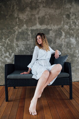 Fototapeta na wymiar a woman in a dress sits on a black sofa against a gray wall