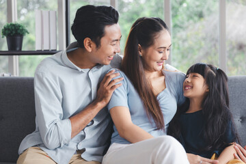 Cheerful young family father mother and daughter smiling embrace sitting on couch in living room at home, Family quality time concept