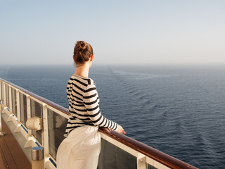 Stylish woman standing on the empty deck of a cruise ship. Sunny morning, clear day. Closeup,...