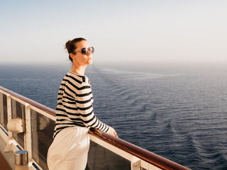 Fototapeta premium Stylish woman standing on the empty deck of a cruise ship. Sunny morning, clear day. Closeup, outdoors. Vacation and travel concept