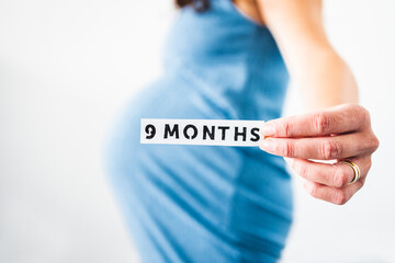pregnant woman holding 9 Months sign towards the camera wearing blue dress in the last month of pregnancy