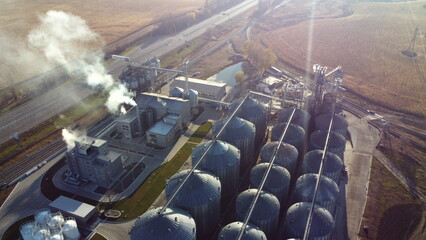 Aerial Drone View Flight Over complex of grain elevator buildings. Metal Round Silos and Metal Barrels for Grain Storage. Drying Storage Harvest. Elevator Tanks and Grain-drying complex. Large Granary