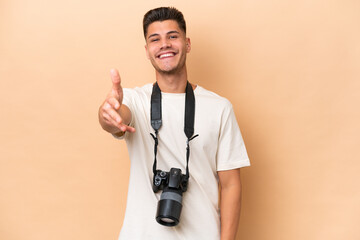 Young photographer caucasian man isolated on beige background shaking hands for closing a good deal