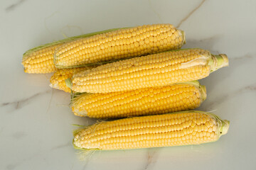 many gold ear of corns vegetable on a white marble background
