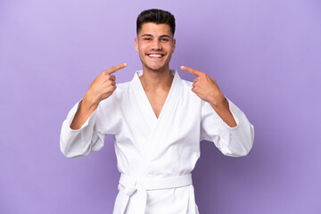 Young caucasian man doing karate isolated on purple background giving a thumbs up gesture